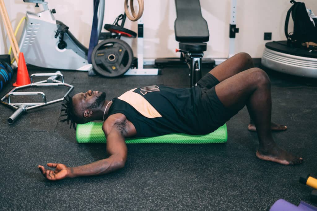 Black attractive strong man Doing an Exercise with Foam Roller on his Upper Back in a gym